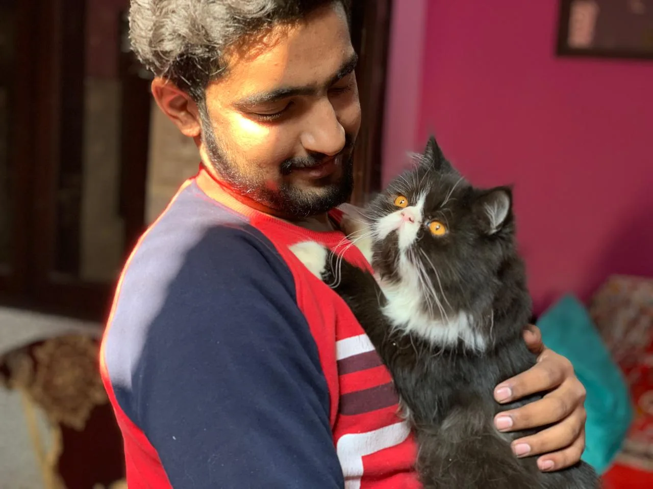 A young man smiling at home while holding his black and white Persian cat