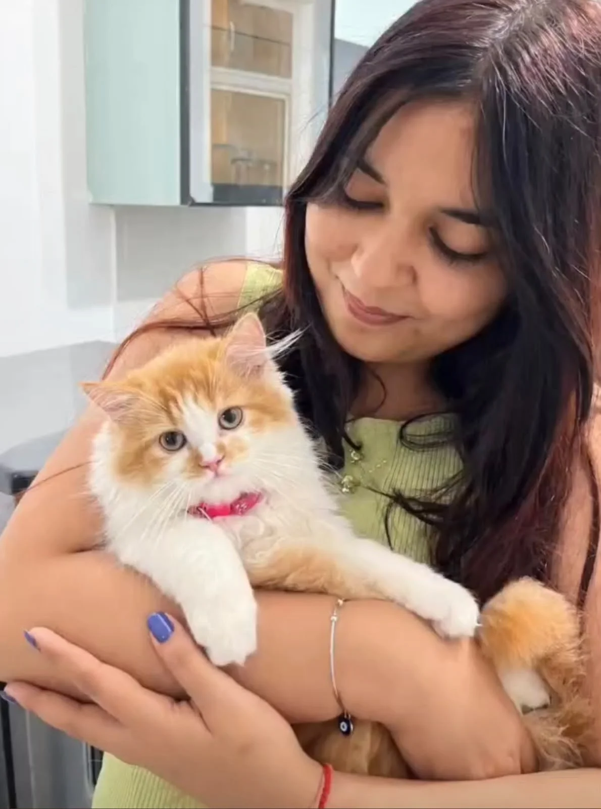 A woman smiling while holding an orange and white Persian cat with a pink collar