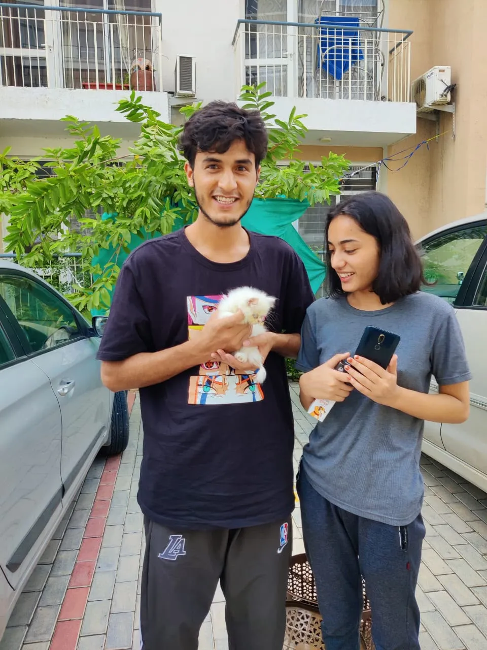 Two new owners smiling as they hold their white Persian kitten outdoors