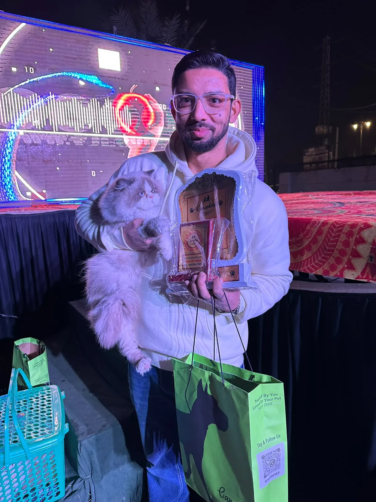 Owner holding a lilac Persian cat next to a pet show trophy