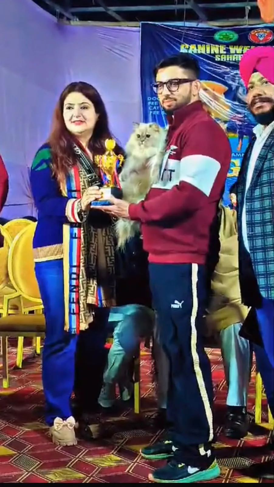 Owner receiving a trophy at a cat show with a cream Persian cat