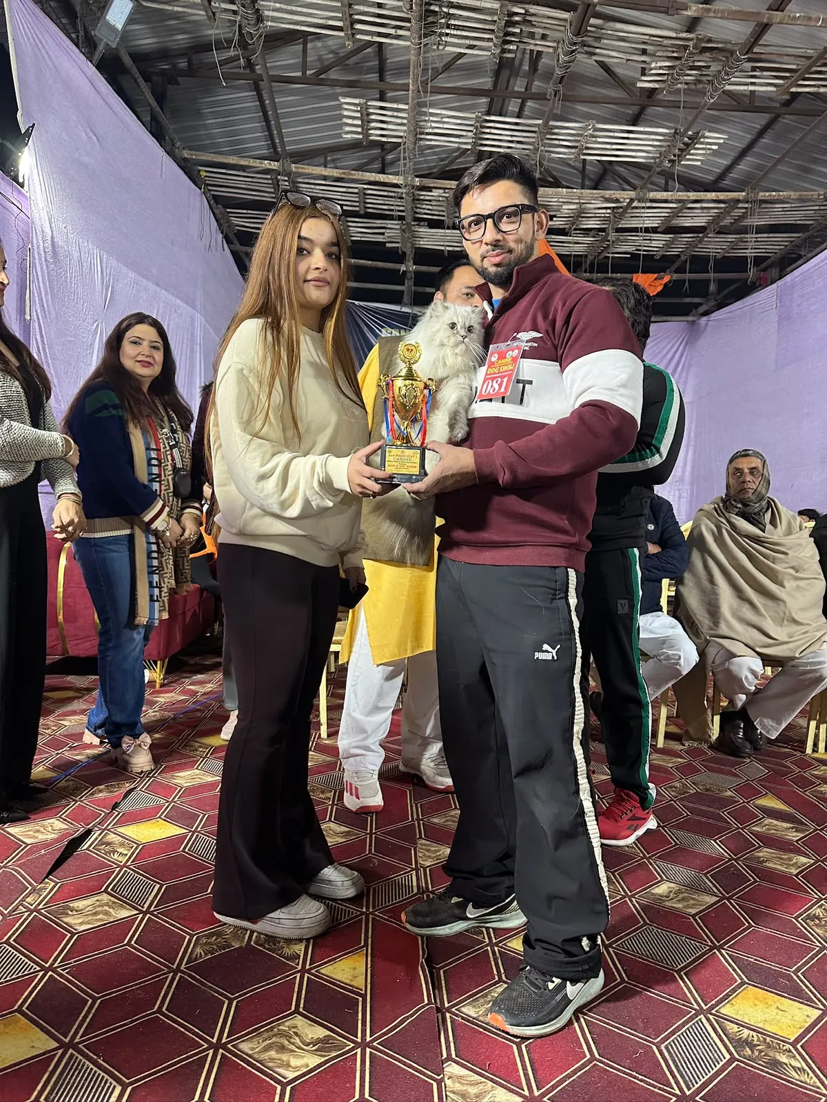 Owner holding a white Persian cat and a gold trophy at a cat show
